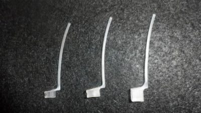 Three small, clear Concha Lock devices with a bent, elongated shape are arranged side by side on a dark textured surface.