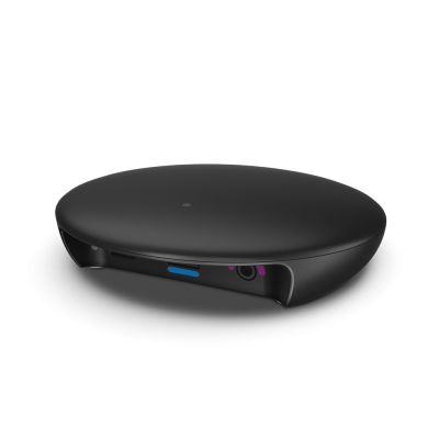 TV Sound is a sleek, black, oval electronic device with a smooth surface and a small circular dot on top. It enhances your TV audio and features ports and buttons on the front edge, all set against a plain white background.